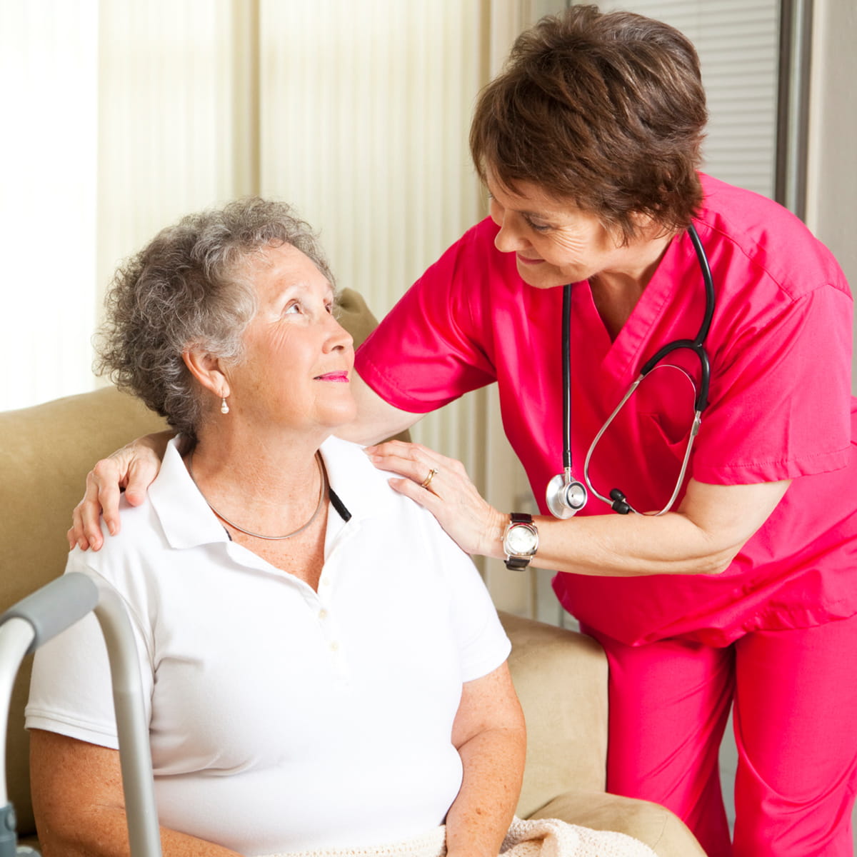 Nurse in pink scrubs looking after an older sitting female patient